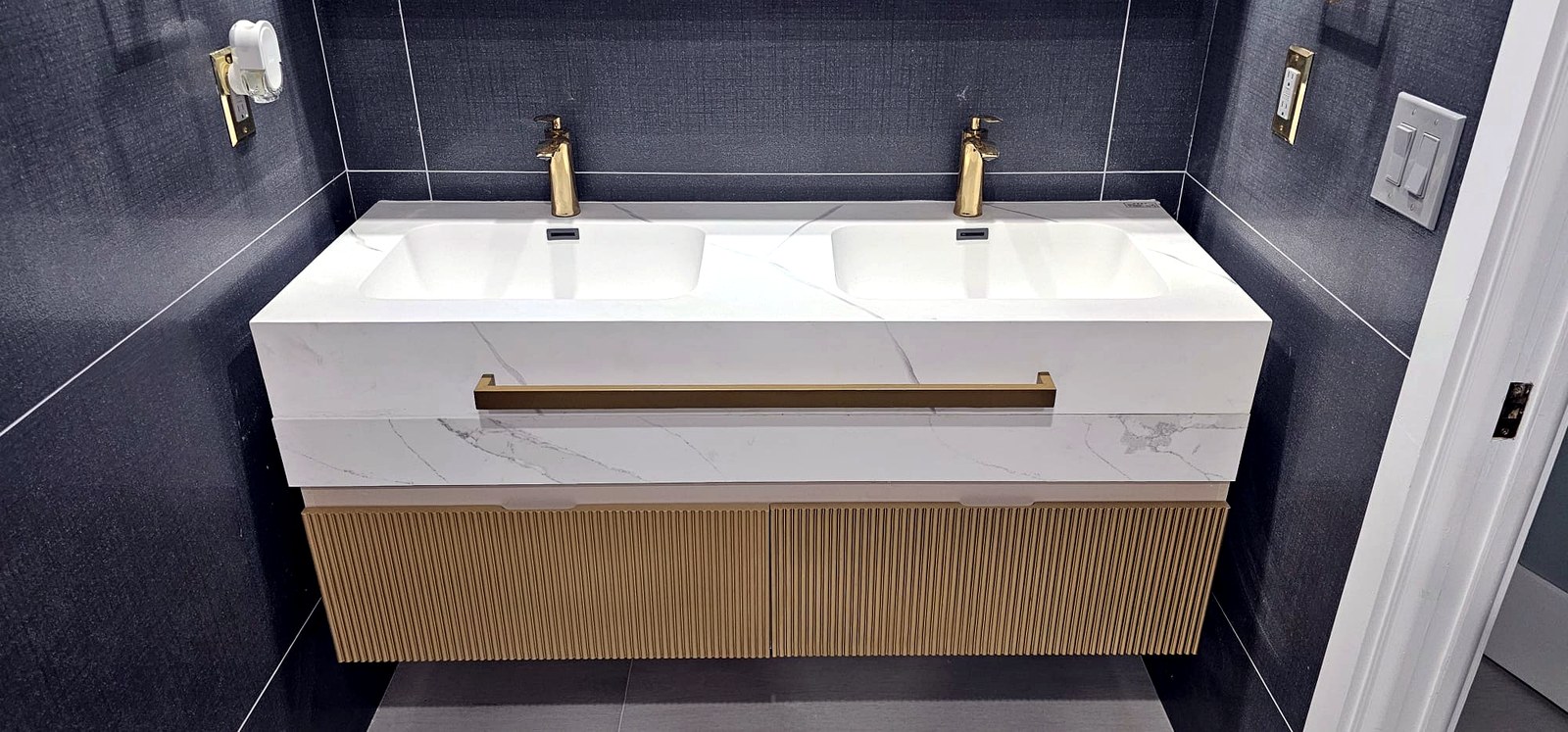 Floating quartz double vanity with fluted wood cabinetry and gold faucets