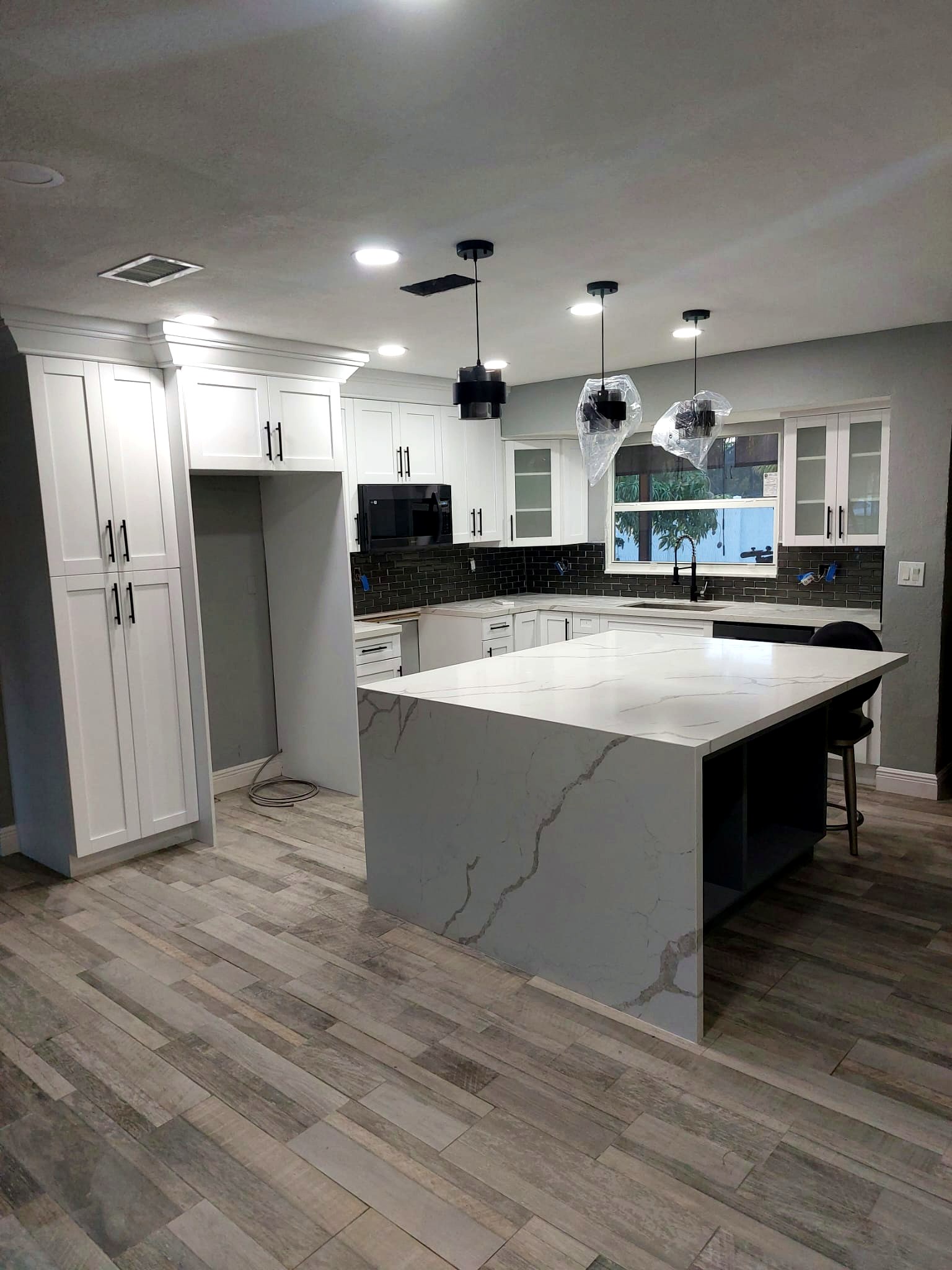 White kitchen with marble waterfall island and wood-look flooring